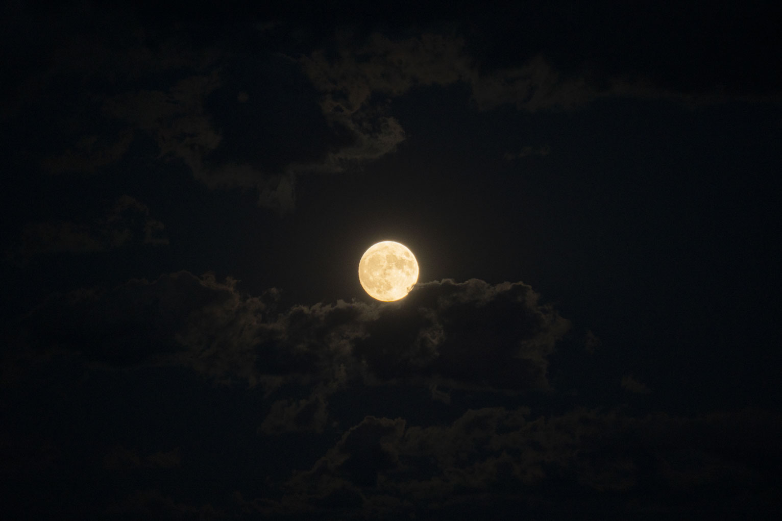 The full moon warm in a dark sky lights some surrounding clouds